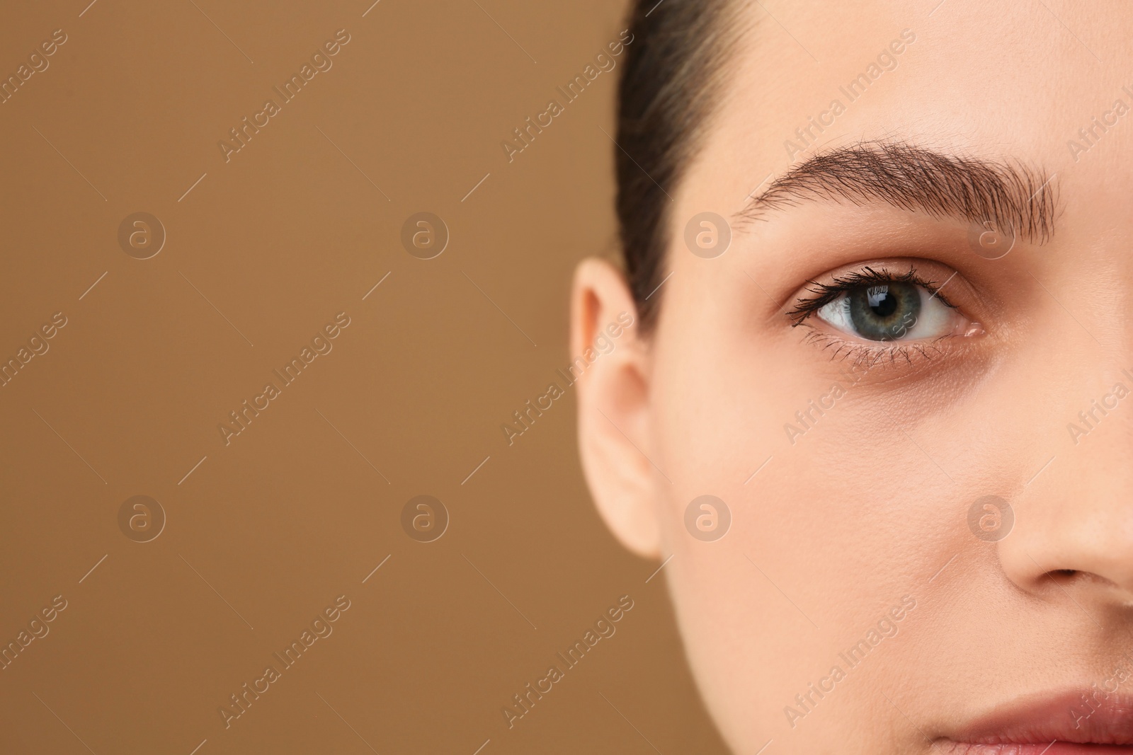 Photo of Young woman with perfect eyebrows on brown background, closeup. Space for text