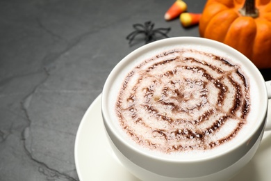 Cup of coffee with spider's net latte art on grey table, closeup. Halloween celebration