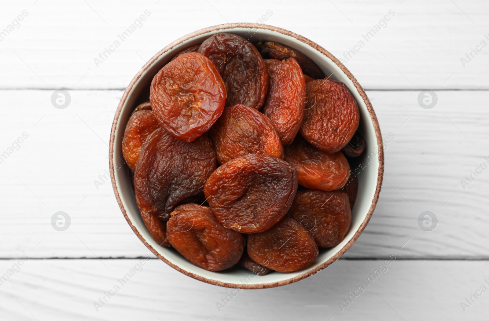 Photo of Bowl of tasty apricots on white wooden table, top view. Dried fruits