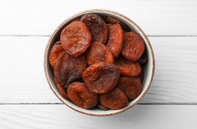 Photo of Bowl of tasty apricots on white wooden table, top view. Dried fruits