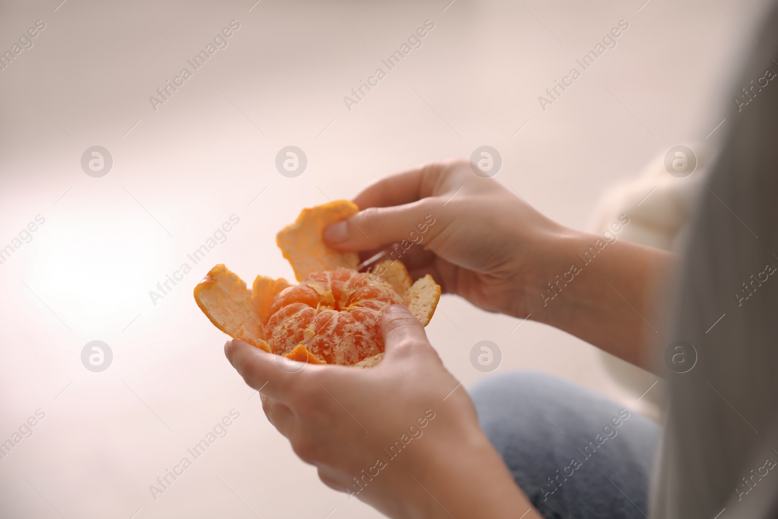 Photo of Woman peeling fresh tangerine on blurred background, closeup