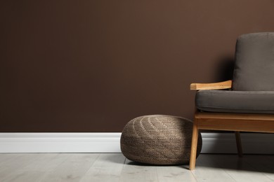 Photo of Stylish knitted pouf and comfortable armchair near brown wall indoors, space for text. Interior design