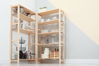 Photo of Wooden shelving units with kitchenware near color wall. Stylish room interior