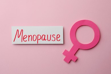 Photo of Card with word Menopause and female gender sign on pink background, flat lay