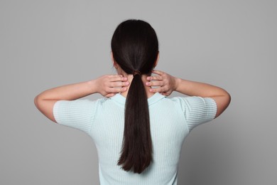 Photo of Young woman suffering from pain in neck on light grey background, back view. Arthritis symptoms