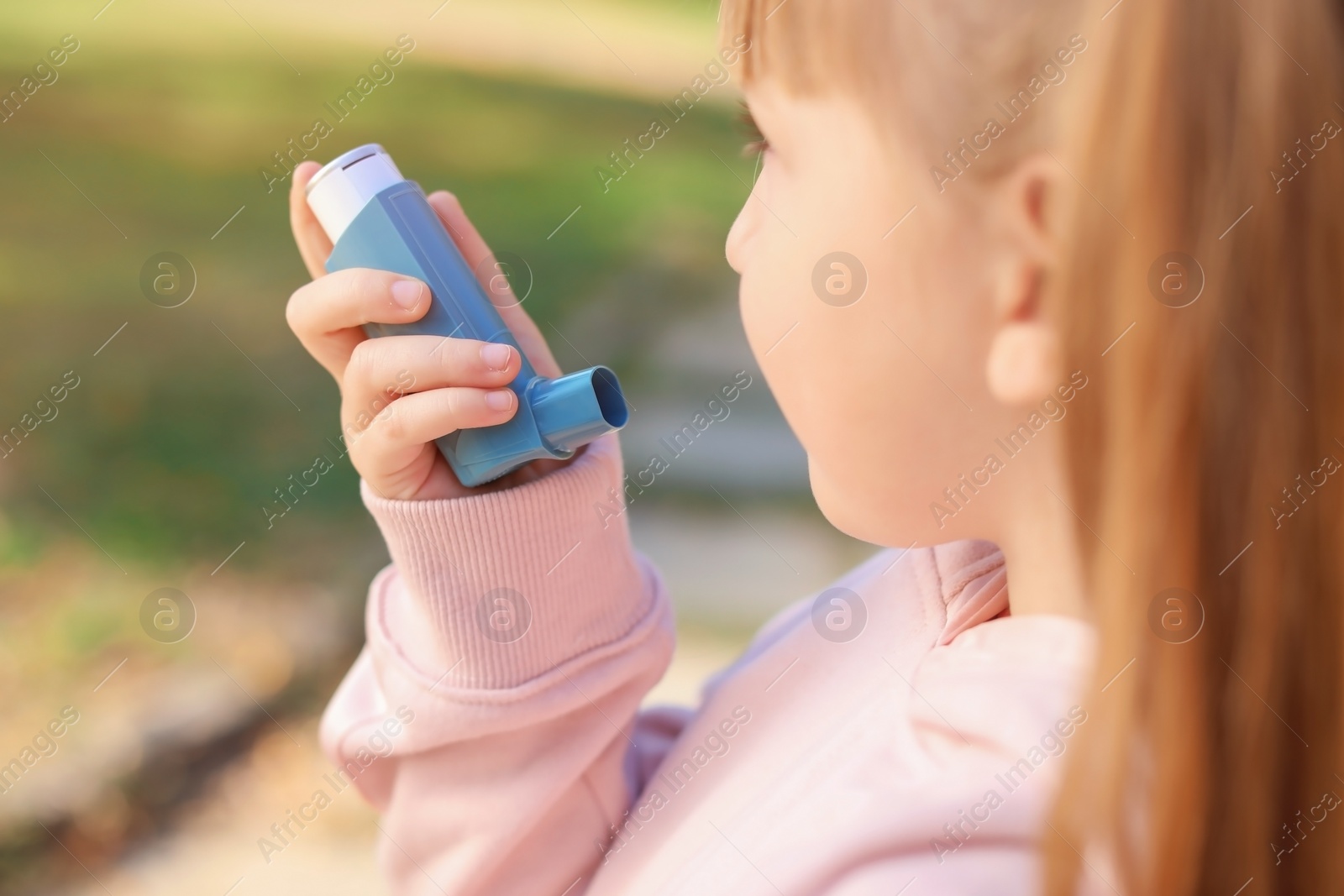 Photo of Little girl using asthma inhaler outdoors. Health care