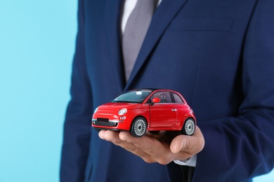 Insurance agent holding toy car on color background, closeup