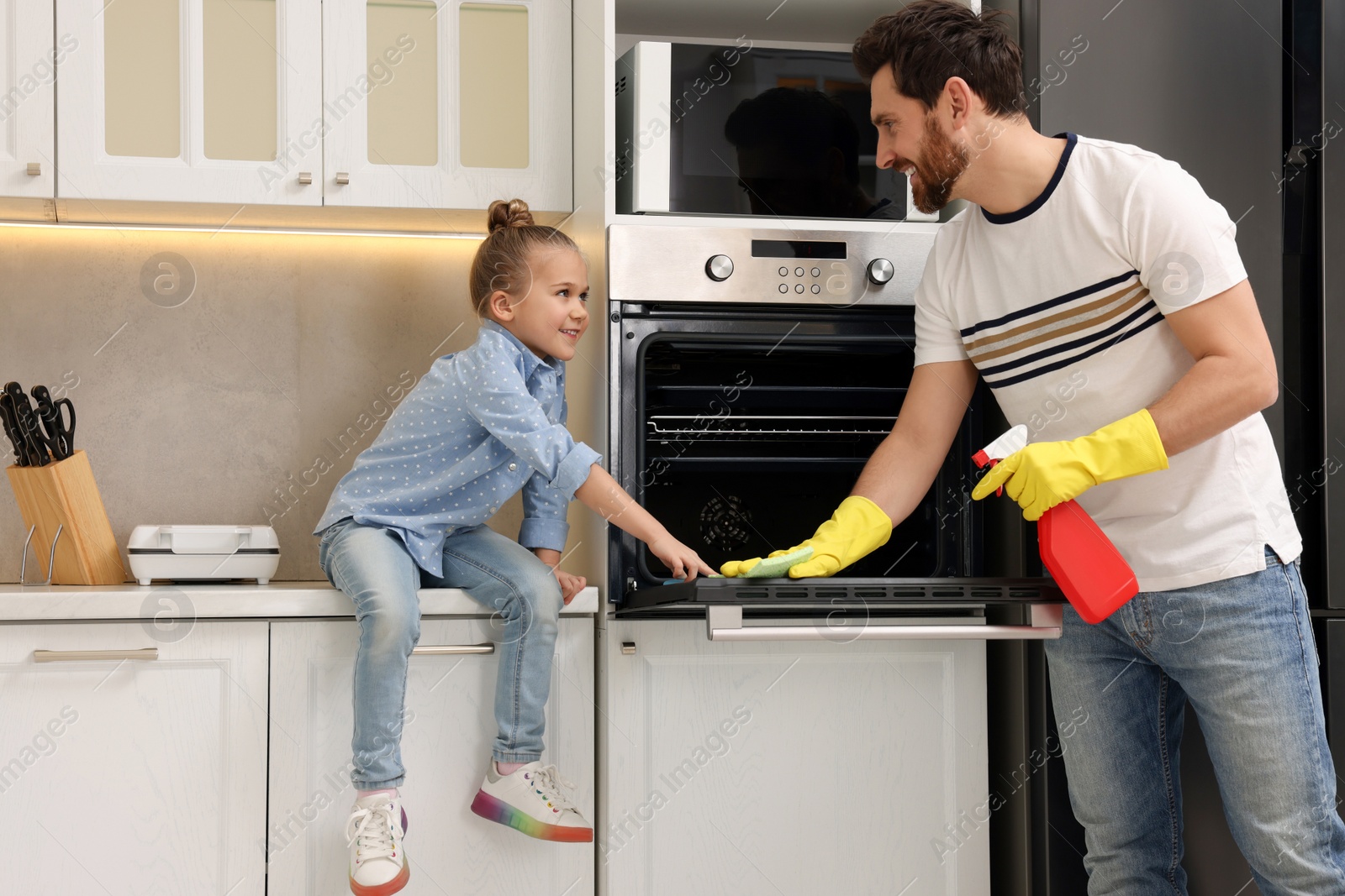 Photo of Spring cleaning. Father and daughter tidying up oven in kitchen together