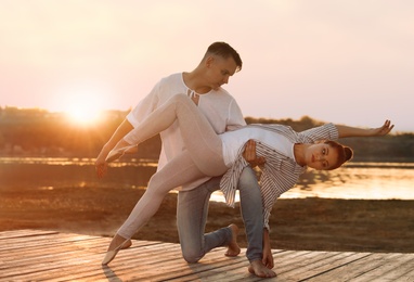 Beautiful young couple practicing dance moves near river at sunset
