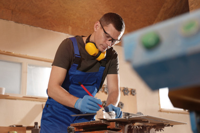 Professional carpenter making mark on wooden bar in workshop