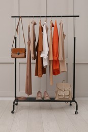 Rack with stylish women's clothes, shoes and accessories near light wall in room