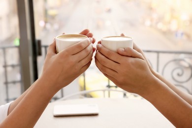 Photo of Friends drinking coffee at wooden table in cafe, closeup