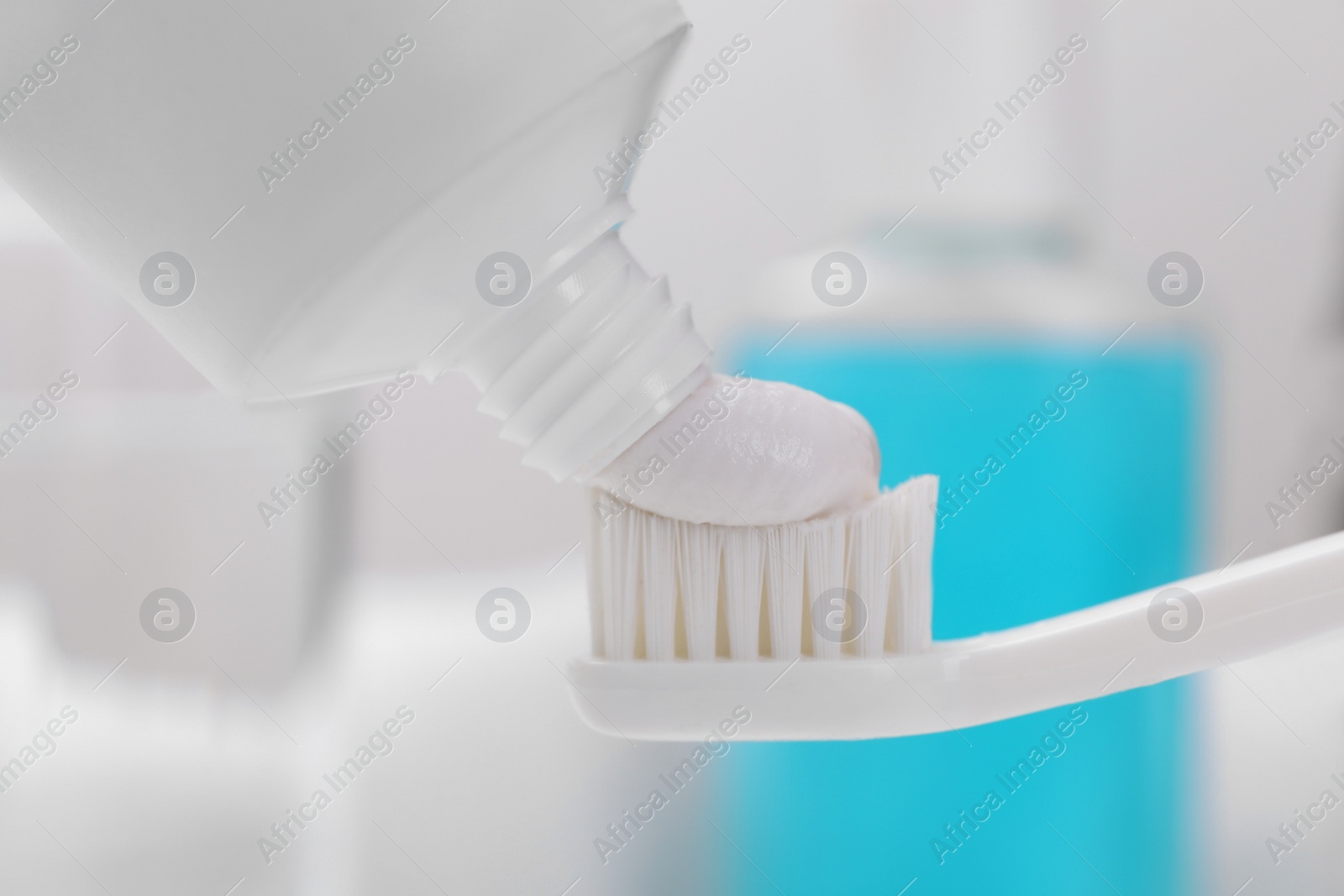 Photo of Squeezing paste onto toothbrush against blurred background, closeup