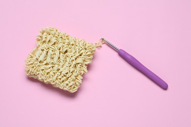 Photo of Instant noodles and crochet hook on pink background, flat lay