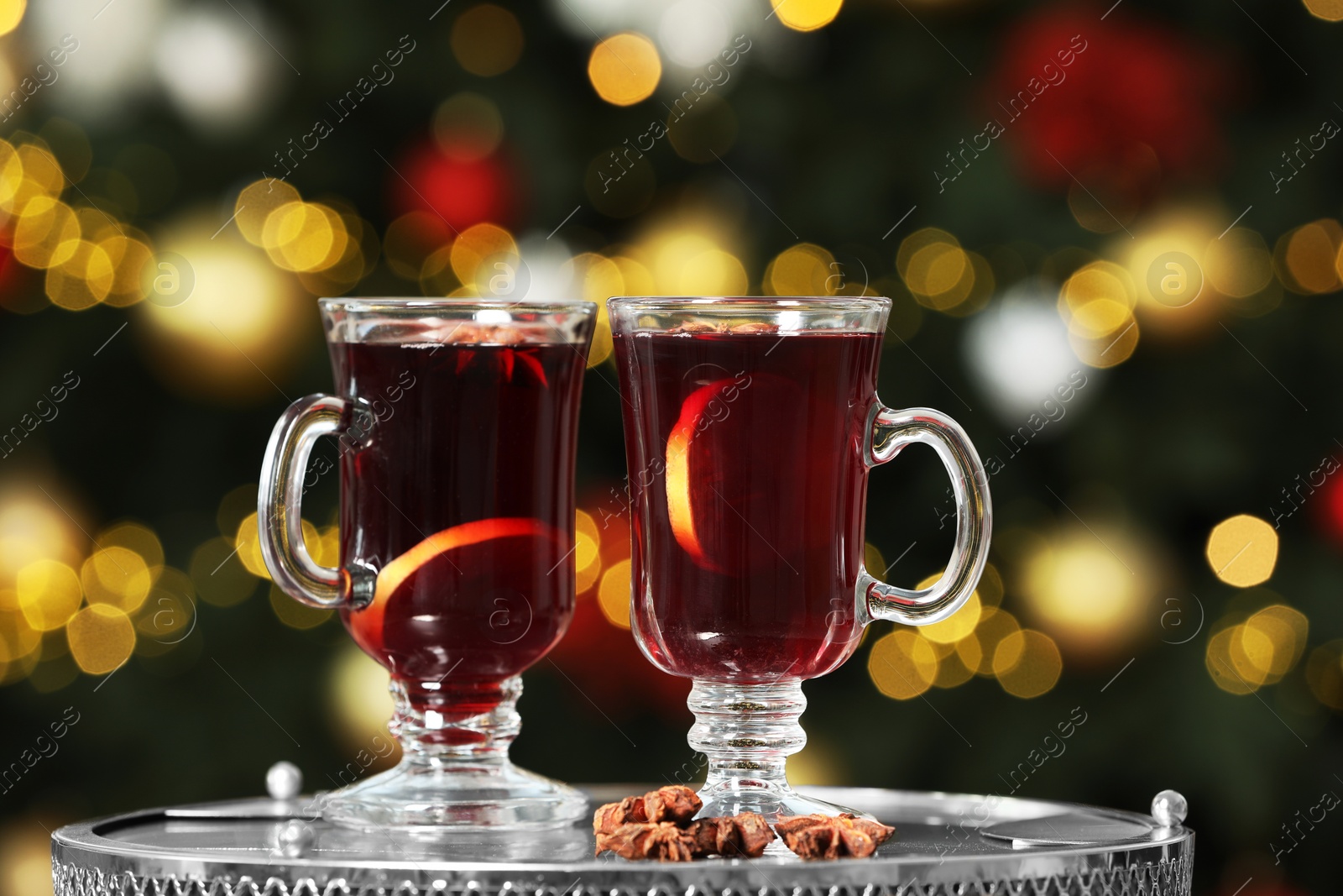 Photo of Hot mulled wine in glass cups and anise stars on table against blurred lights