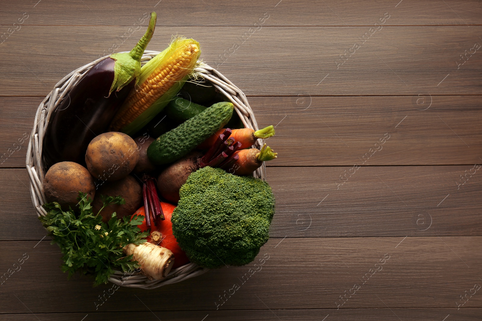 Photo of Basket with different fresh ripe vegetables on wooden table, top view. Space for text