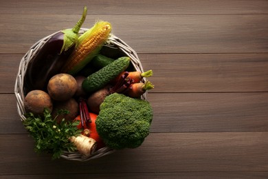 Basket with different fresh ripe vegetables on wooden table, top view. Space for text