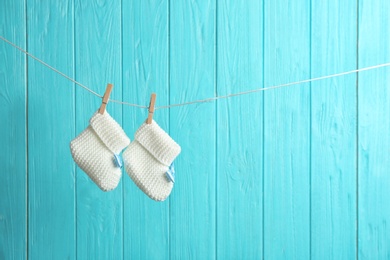 Baby booties on laundry line against color wooden background, space for text. Child accessories