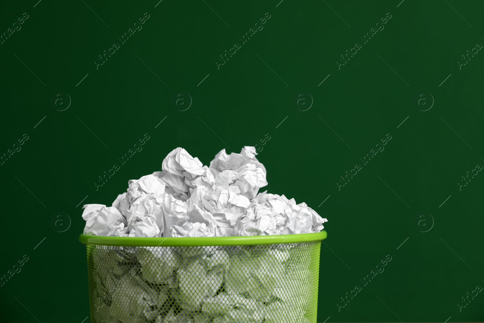 Photo of Metal bin with crumpled paper on color background, space for text