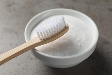Bamboo toothbrush and bowl of baking soda on grey table, closeup