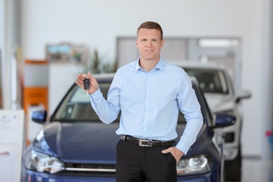Photo of Handsome young salesman holding key in car dealership