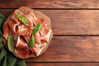 Photo of Slices of tasty cured ham and basil on wooden table, top view. Space for text
