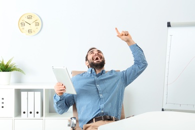 Photo of Emotional young man with tablet celebrating victory in office