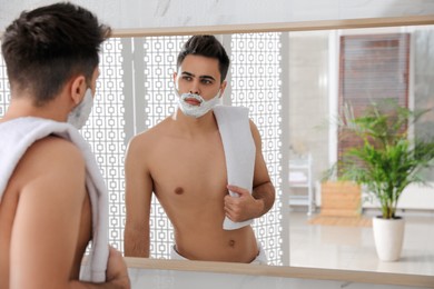 Handsome young man with shaving foam near mirror in bathroom, space for text