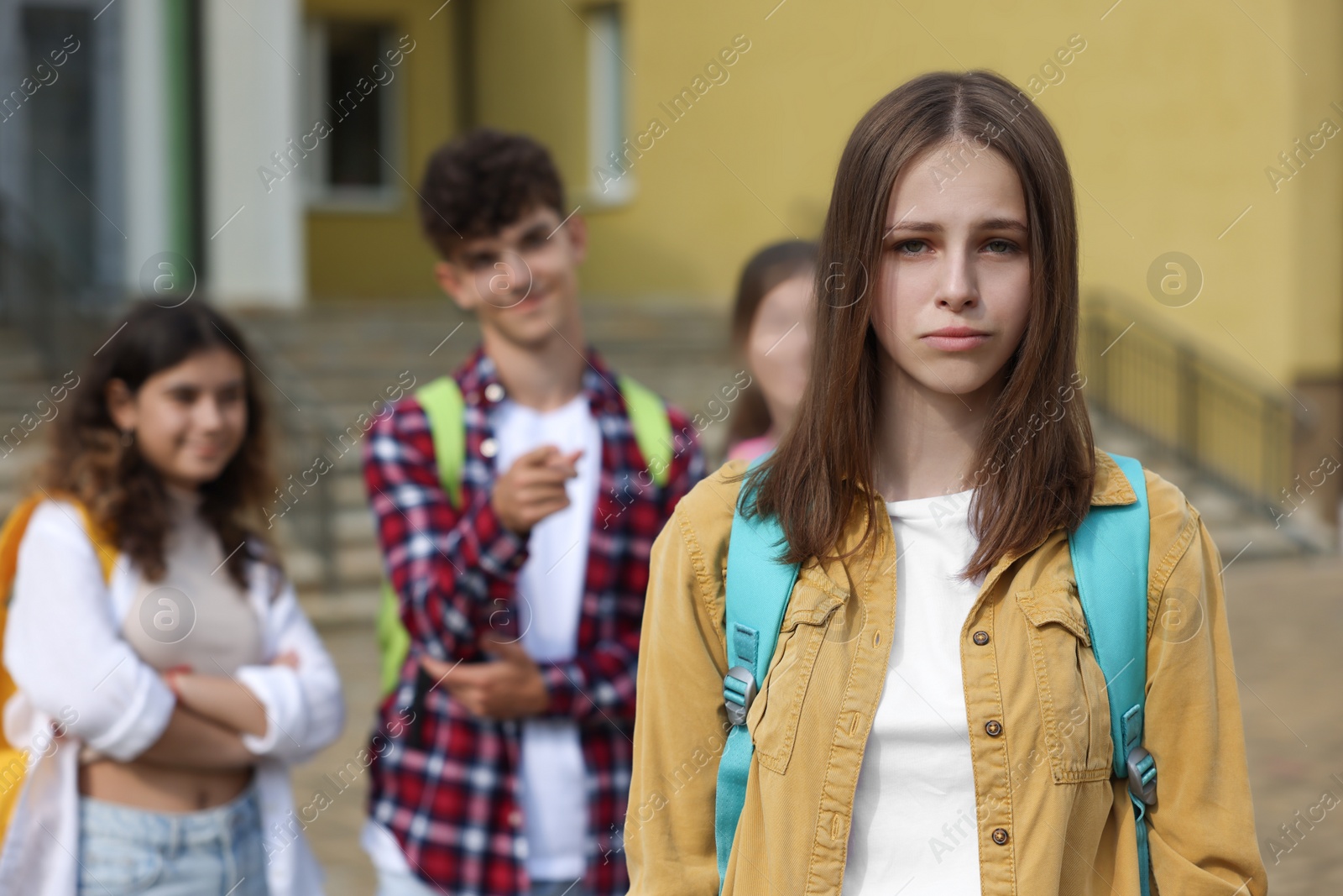 Photo of Teen problems. Lonely girl standing separately from other students outdoors