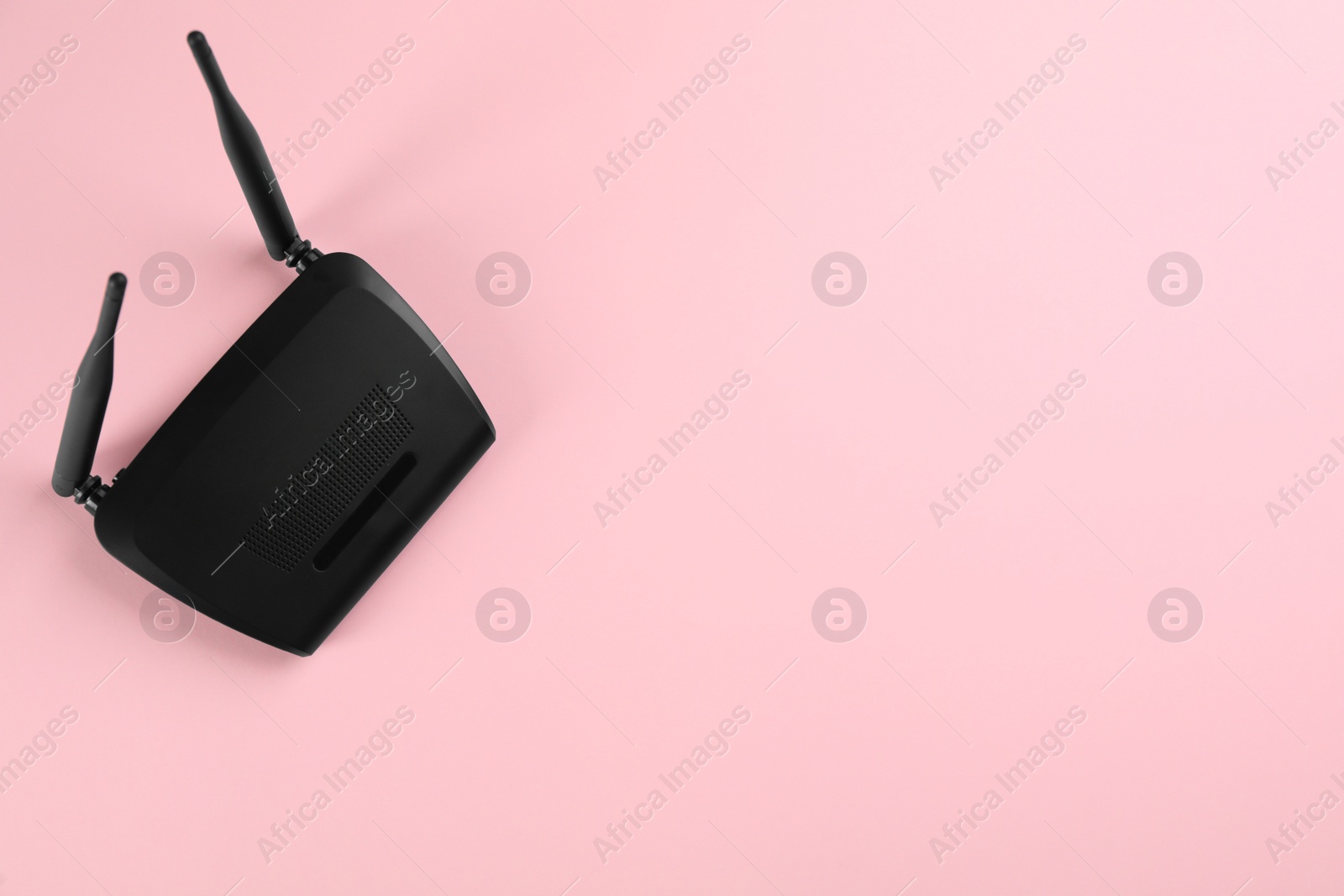 Photo of Modern Wi-Fi router on light pink background, top view. Space for text