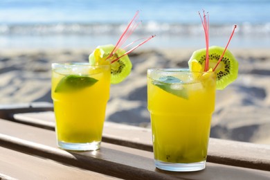 Photo of Glasses of refreshing drink with kiwi and mint on wooden bench near sea