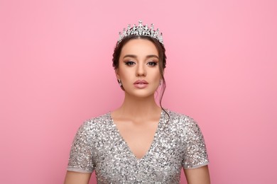 Beautiful young woman wearing luxurious tiara on pink background