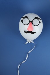 Photo of Man's face made of balloon, fake mustache, nose and glasses on blue background, top view