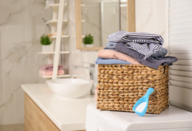 Wicker basket with laundry and detergent on washing machine in bathroom. Space for text