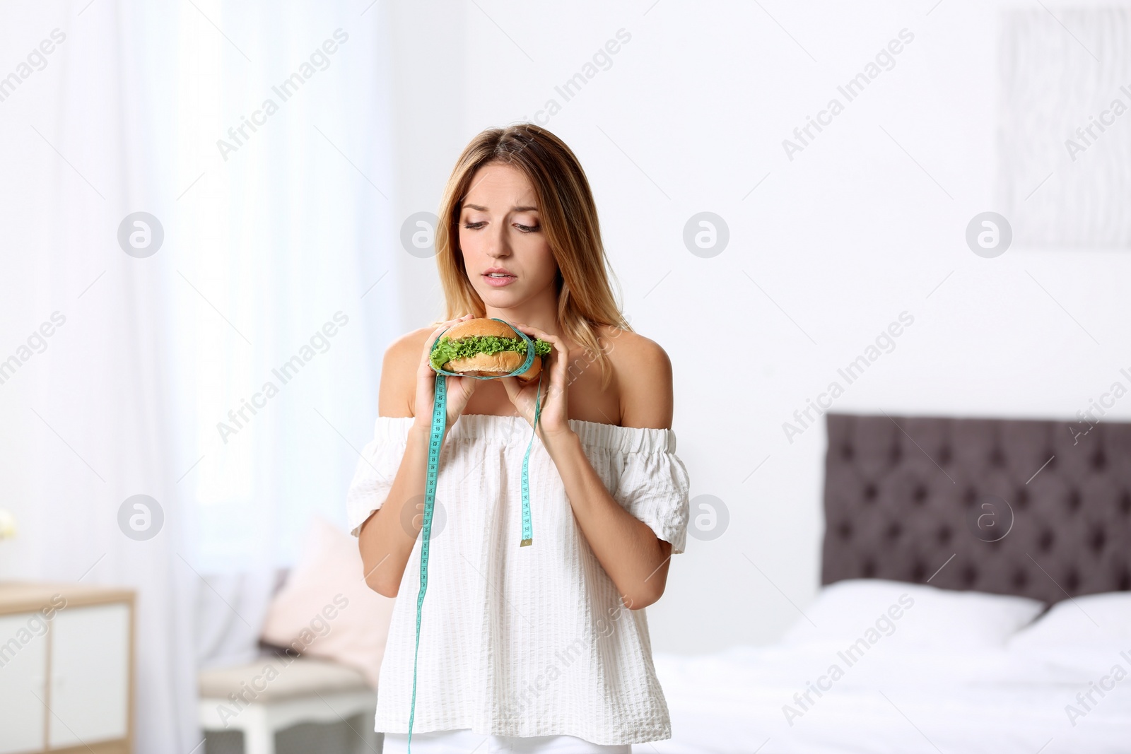 Photo of Young woman with measuring tape and burger at home. Weight loss diet