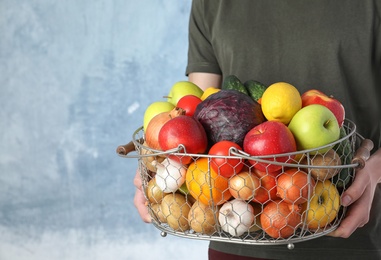 Photo of Man holding basket full of fresh  vegetables and fruits against color background, closeup. Space for text