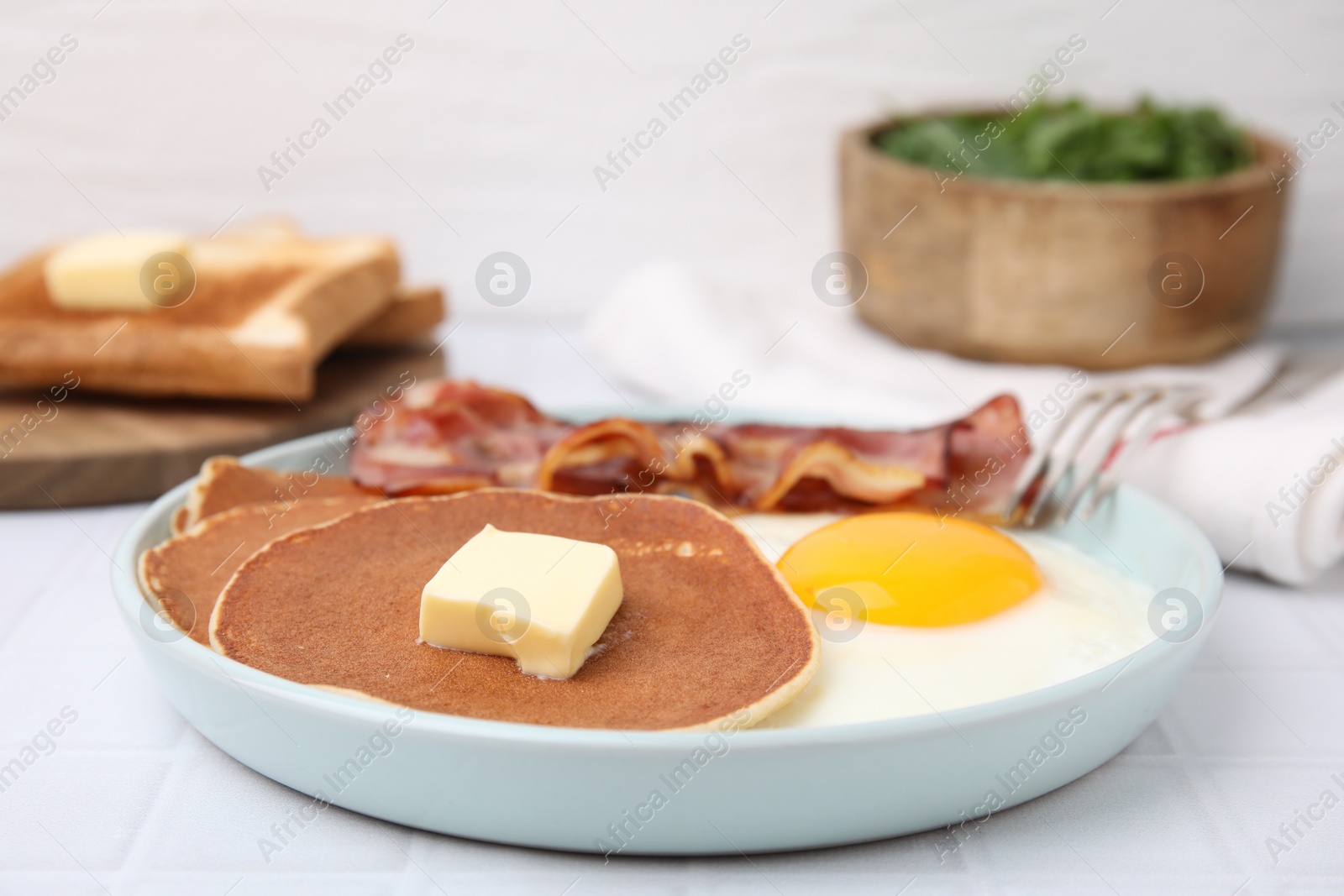 Photo of Tasty pancakes served with fried egg and bacon on white tiled table, closeup