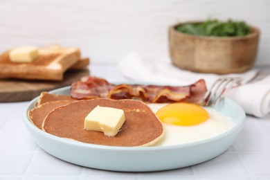 Tasty pancakes served with fried egg and bacon on white tiled table, closeup