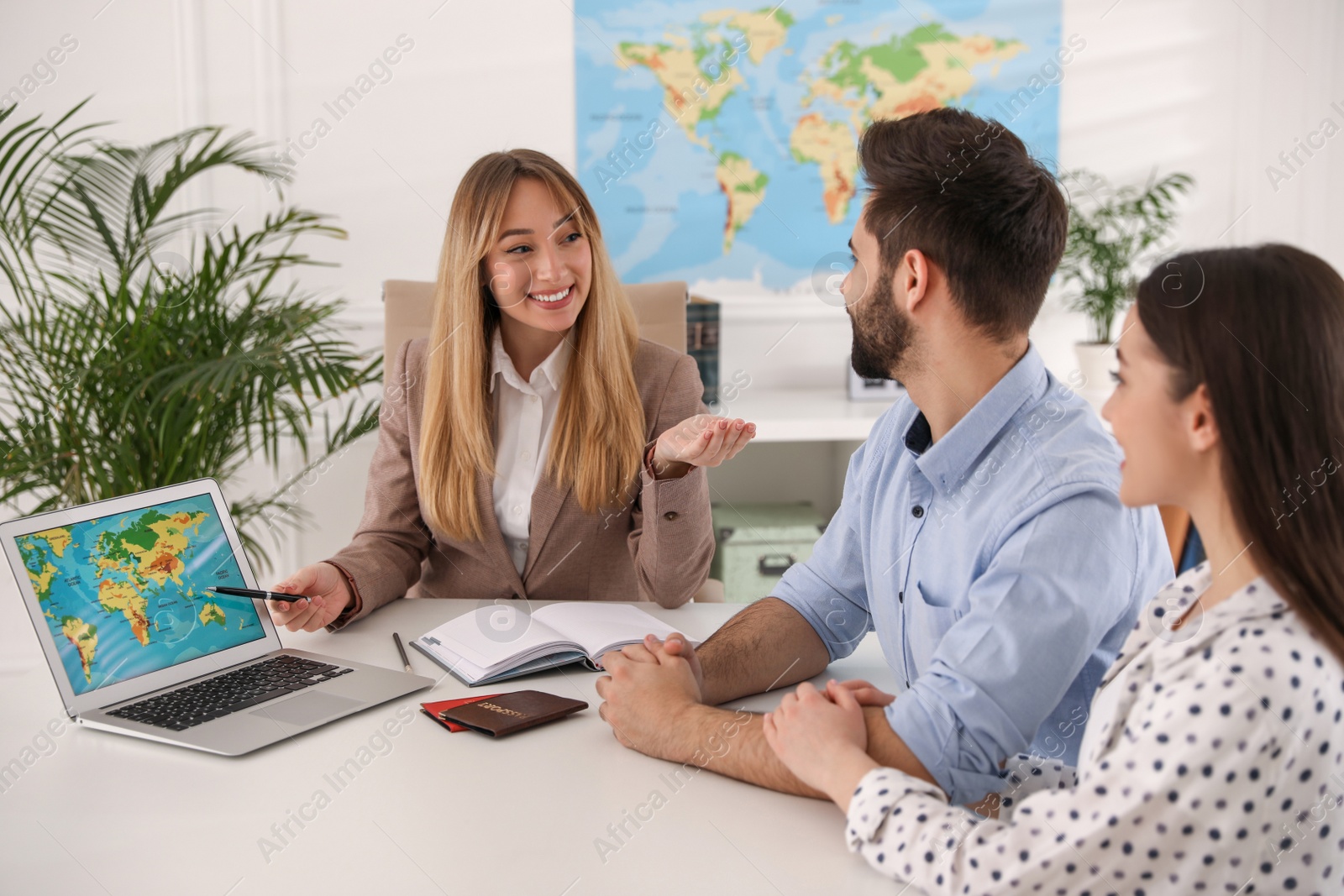 Photo of Manager showing map to couple on laptop at desk in travel agency