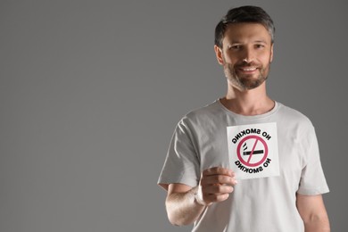 Photo of Man holding card with no smoking sign on gray background, selective focus. Space for text