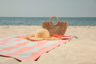 Beach towel with bag, hat and book on sand near sea