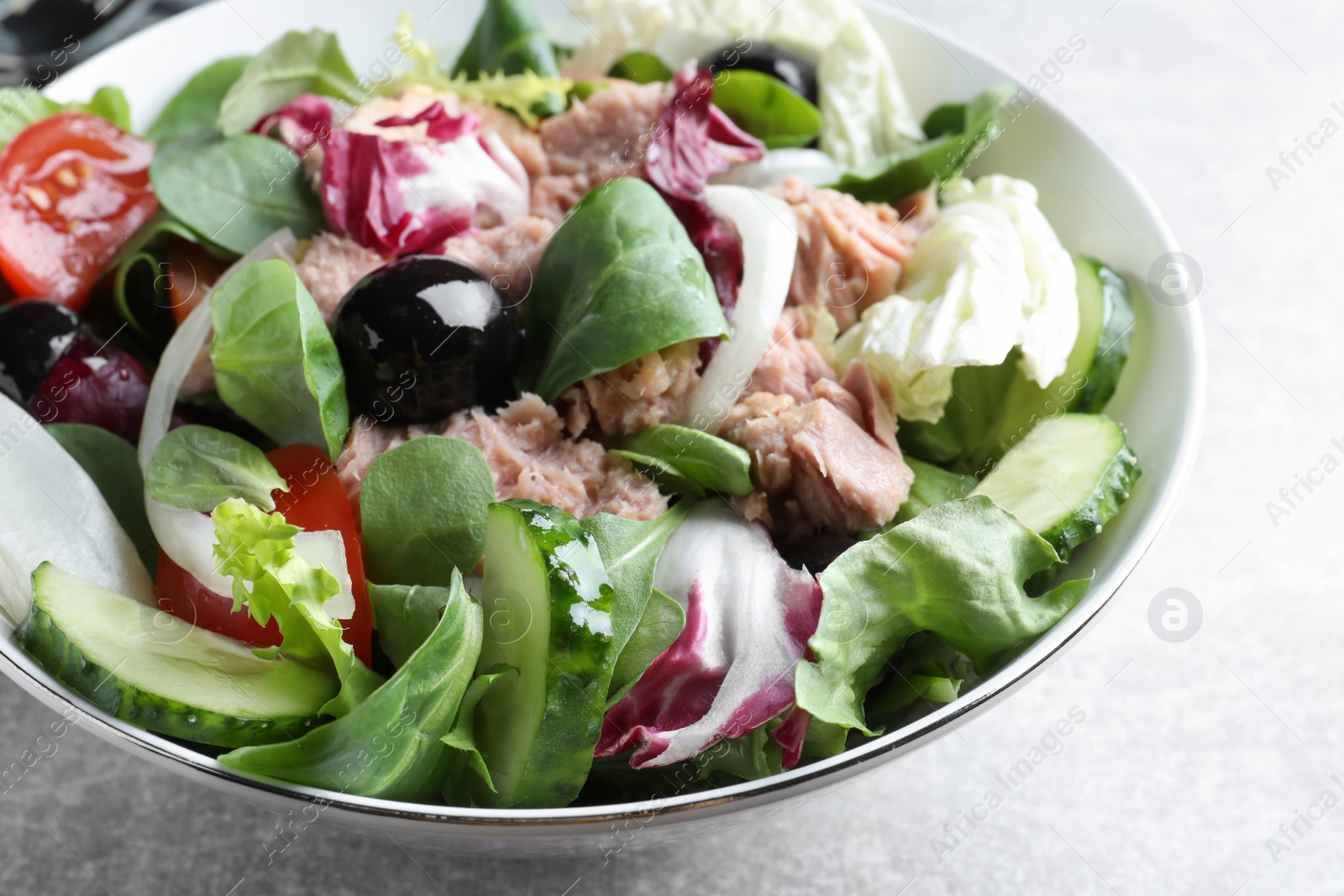 Photo of Bowl of delicious salad with canned tuna and vegetables on light grey table, closeup