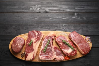 Pieces of raw beef meat and spices on black wooden table, top view. Space for text