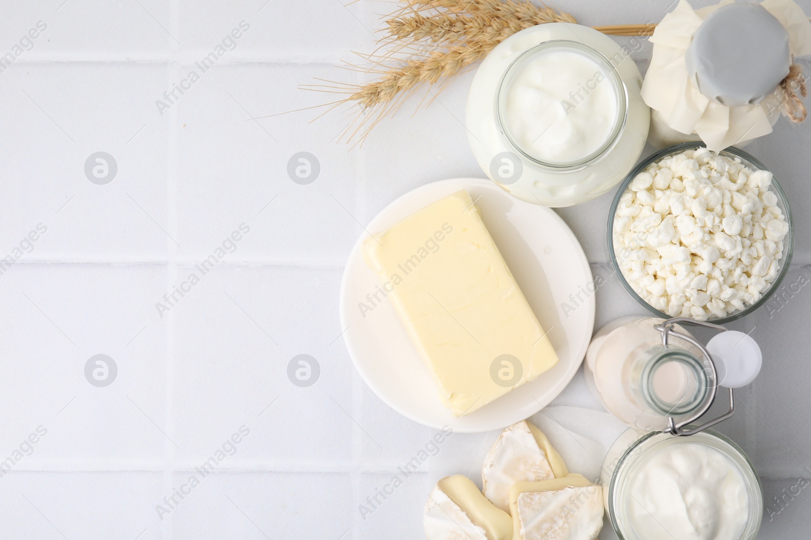 Photo of Different dairy products and spikes on white tiled table, flat lay. Space for text