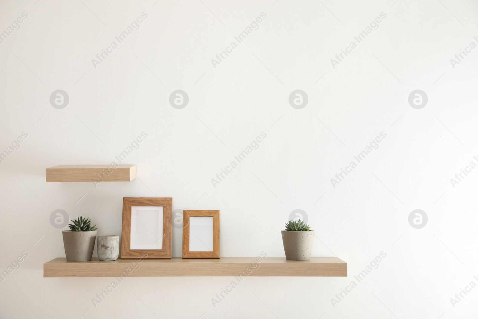 Photo of Wooden shelves with plants and photo frames  on light wall