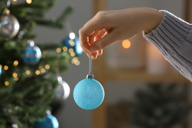 Woman holding festive ball near Christmas tree indoors, closeup