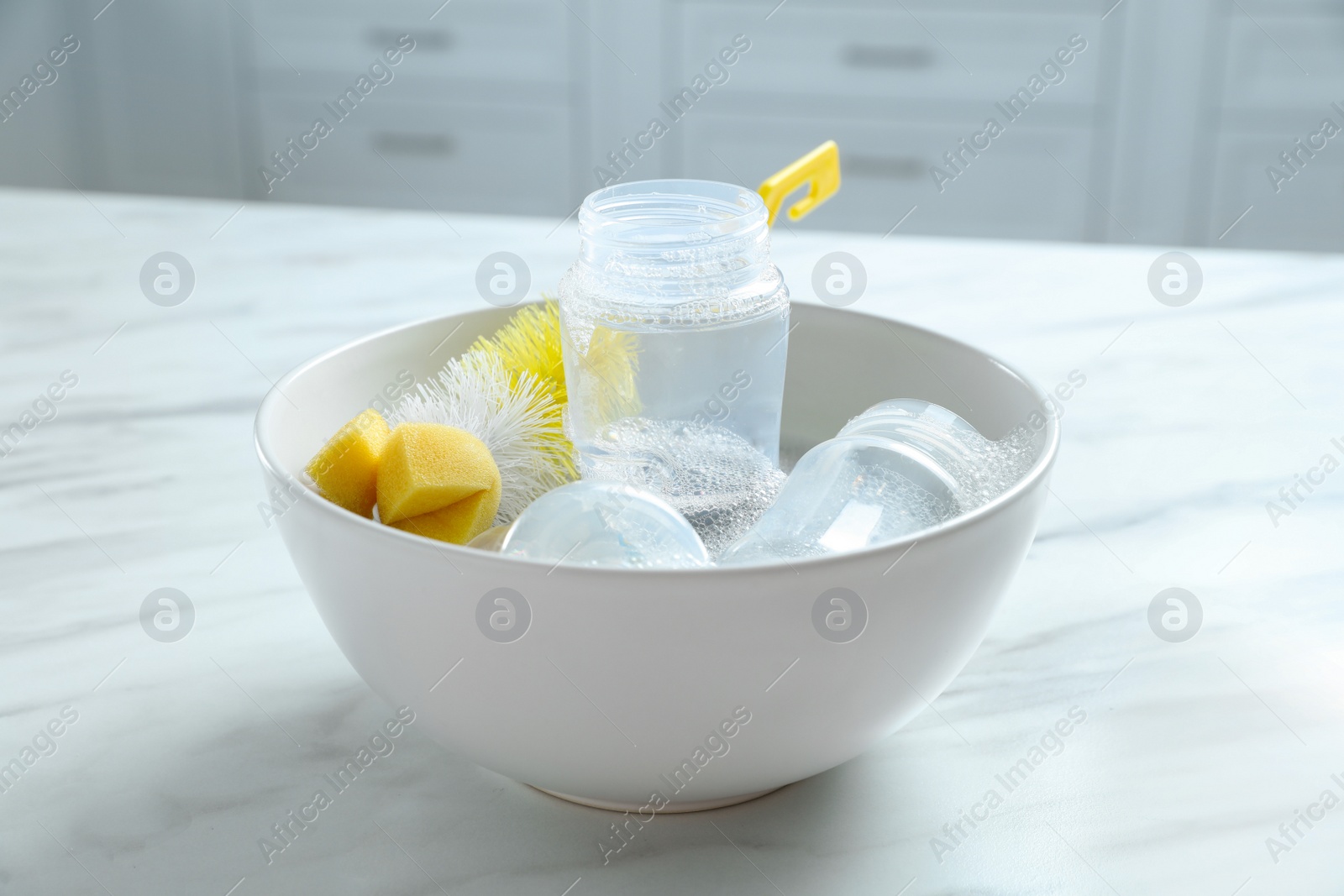 Photo of Bowl with baby bottles and cleaning brush on white marble table in kitchen