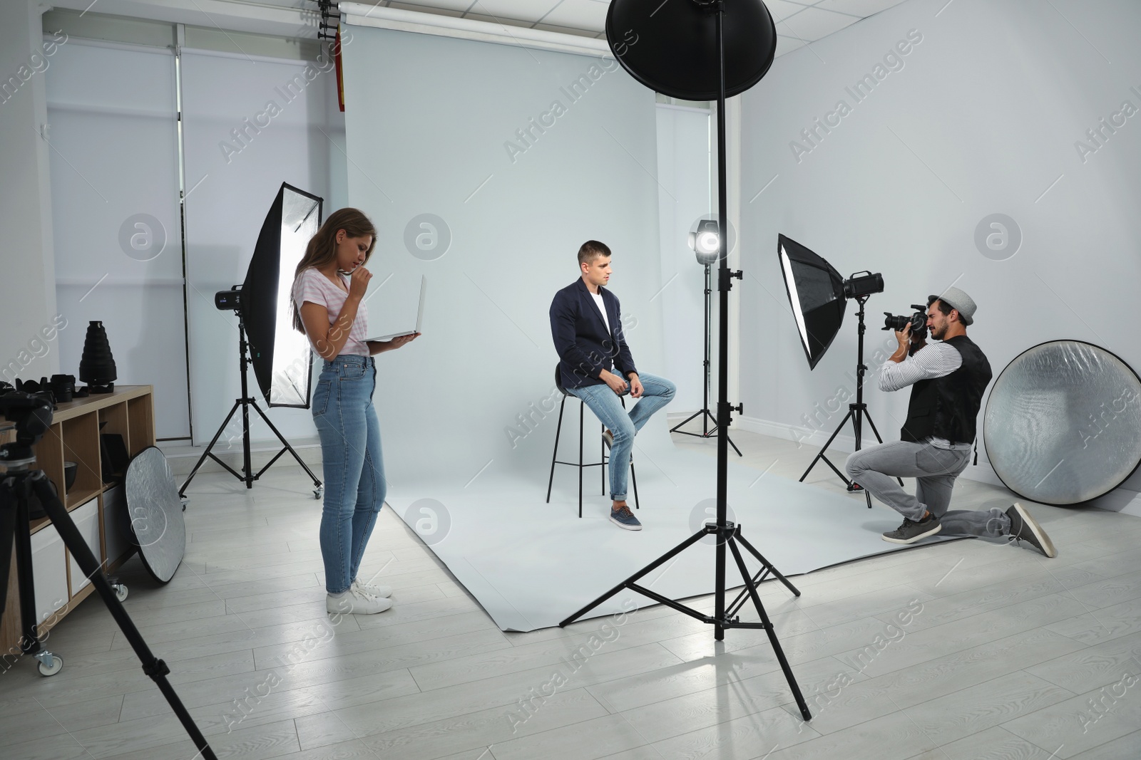 Photo of Professional photographer with assistant taking picture of young man in modern studio