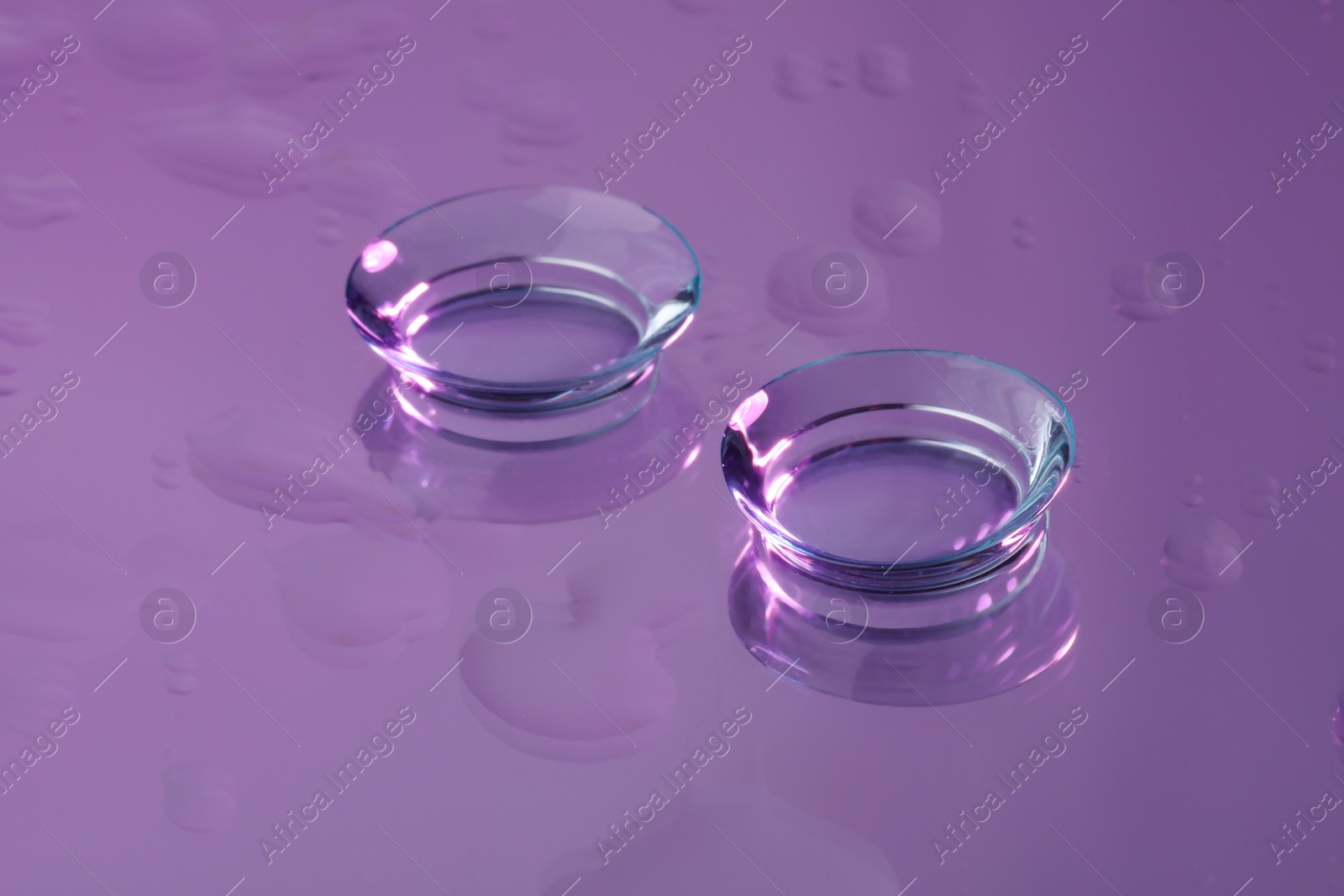 Photo of Pair of contact lenses on wet violet reflective surface