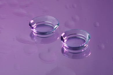 Photo of Pair of contact lenses on wet violet reflective surface